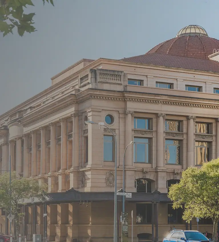 Historic sandstone courthouse building with classical columns and a red domed roof, surrounded by trees and parked cars.